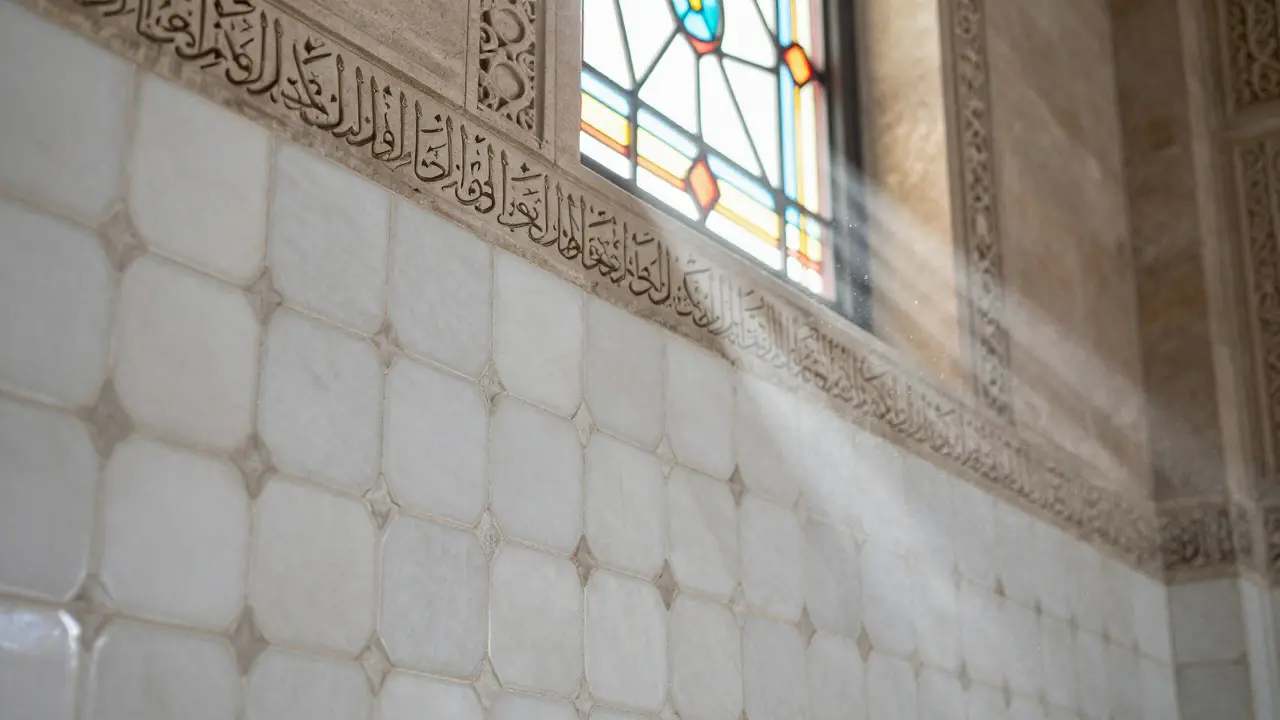 Close-up of hand-laid tile mosaic and carved Quranic script on white limestone wall.