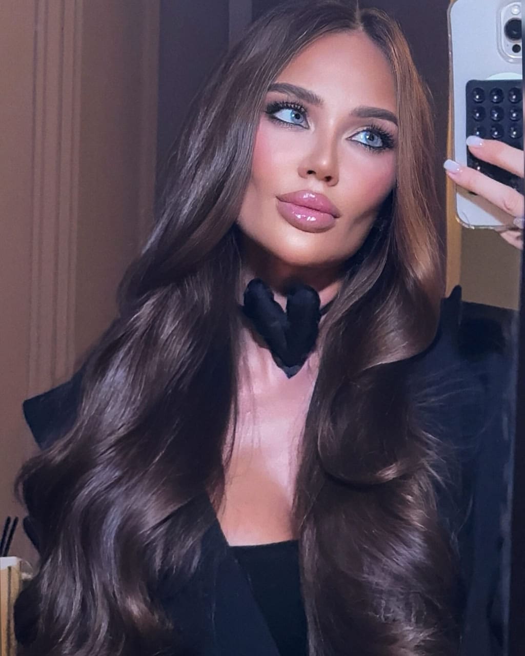 Mirror selfie of woman in black blazer and choker holding a smartphone in her right hand.