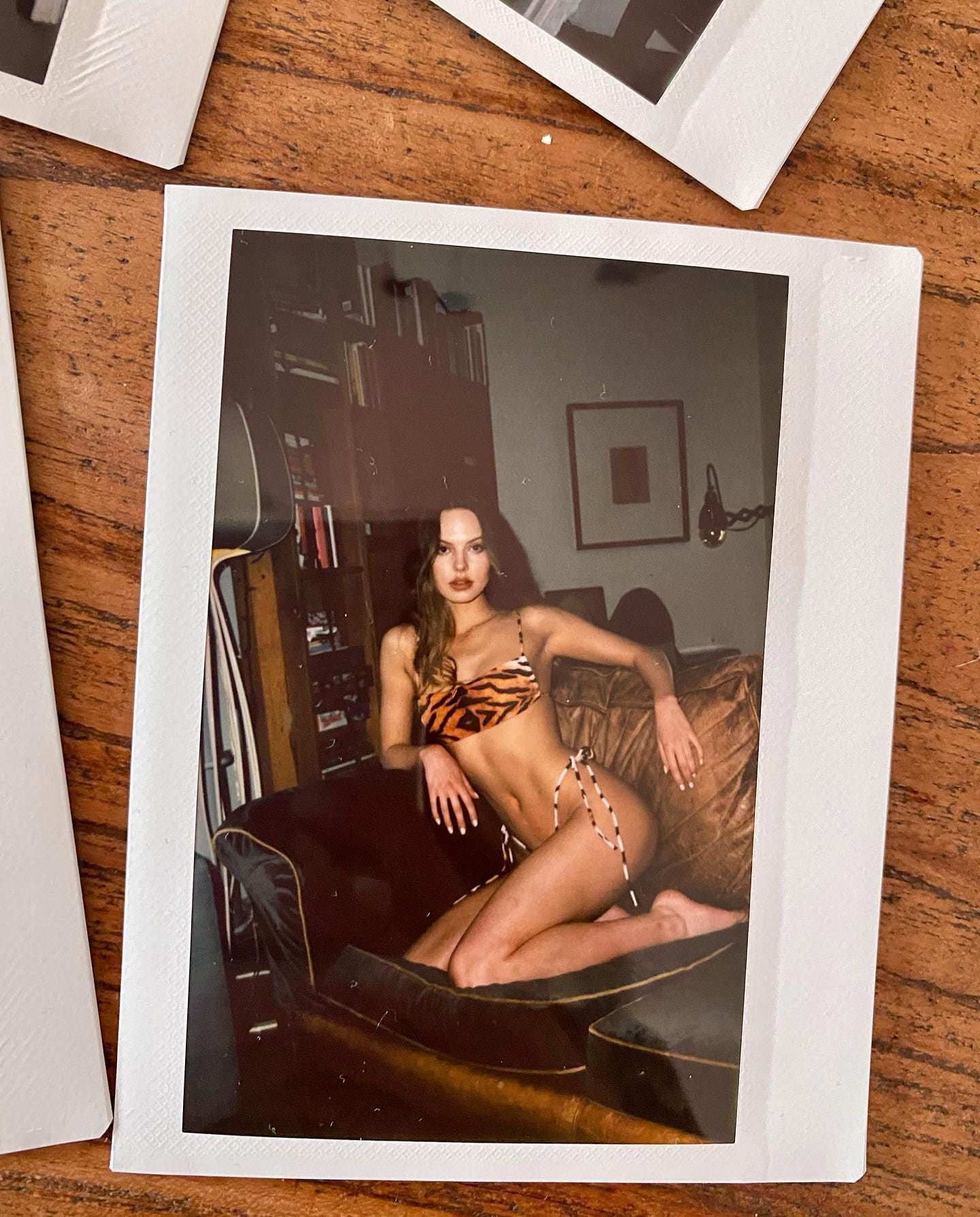 A woman sits on a brown leather sofa in a library-like room, wearing a patterned two-piece outfit.
